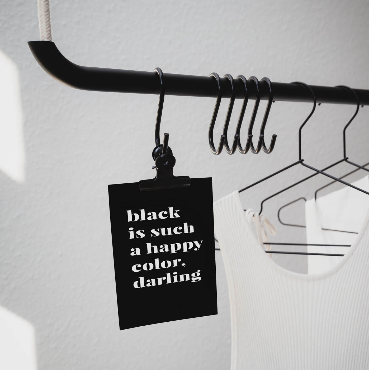 Kleiderstange an der eine Postkarte hängt auf der steht: "black is such a happy color, darling"