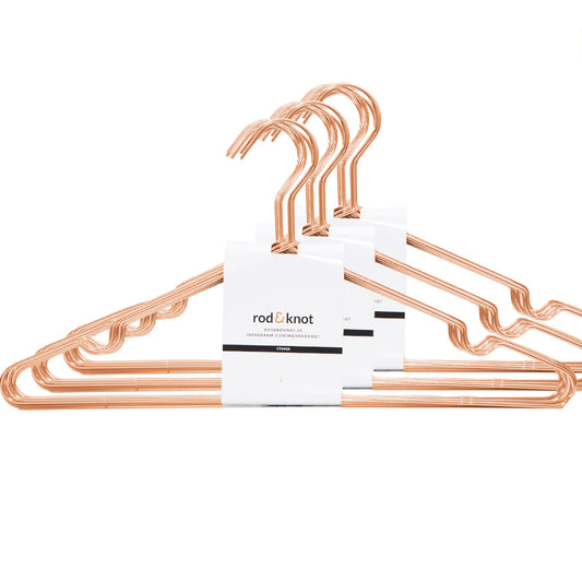 Ein Set aus drei kupferfarbenen Drahtbügeln mit überlappenden Haken. Die Bügel sind in ein weißes Papierband mit der Aufschrift „rod & knot“ eingewickelt und als „Kleiderbügel aus stabilem Metall (Sparsets)“ beschrieben. Diese Kleiderbügel aus stabilem Metall (Sparsets) von rod & knot bestechen durch ihr schlichtes, minimalistisches Design, das den ästhetischen Reiz betont und gleichzeitig platzsparende Aufbewahrung bietet.